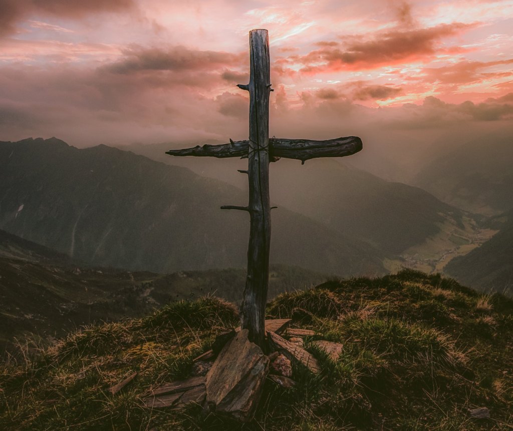 Kreuz auf dem Berg mit leicht rötlichen Wolken