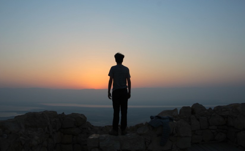 Die Silhouette eines Mannes steht auf einer Mauer und schaut hinab.